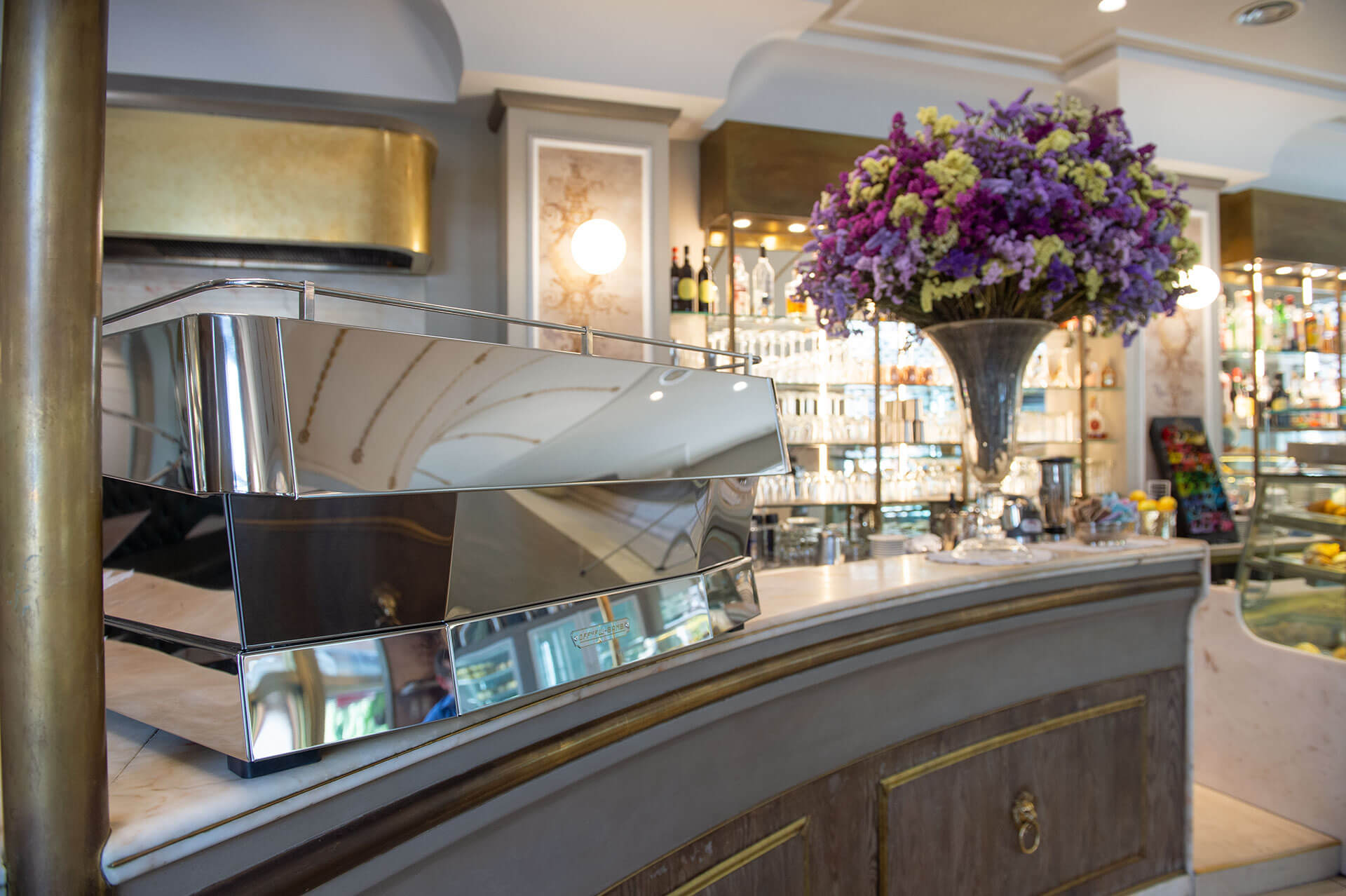 A polished OFB espresso machine on marble countertop next to a great bouquet of purple flowers